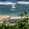 Aerial view of a tropical beach with lush greenery and turquoise ocean waves.