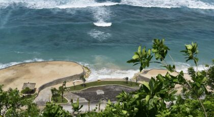 Aerial view of a tropical beach with lush greenery and turquoise ocean waves.