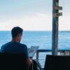 A man relaxes with a book overlooking the ocean in Bali, enjoying leisure time.
