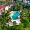 Aerial view of a luxury resort featuring a swimming pool, villas, and lush palm trees.