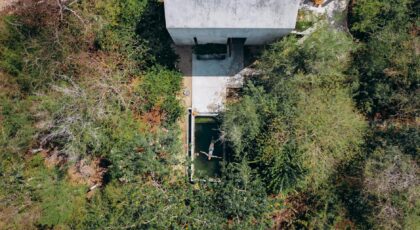Aerial shot of a modern house with a pool amidst lush greenery, conveying tranquility.