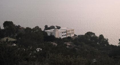 Charming villa nestled on a hill with a serene sea view, surrounded by lush greenery.