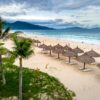 Picturesque tropical beach with palm trees and umbrella huts on a cloudy day.