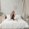 Young woman enjoying a skincare routine in a minimalist bedroom, surrounded by nature-inspired decor.
