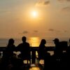 Silhouettes of people enjoying a Bali sunset at a beachside bar, perfect vacation vibe.