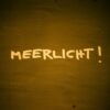Graffiti reading 'Meerlicht' on a dark textured wall in warm lighting.