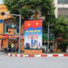 Vibrant Hà Nội street scene featuring a New Year 2026 billboard, motorcycles, and colorful shops.