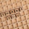 Wooden letter tiles spelling 'thank you' on a grid background, perfect for gratitude themes.