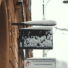 A snow-covered sign along a historic street in Krakow, Poland, during winter.