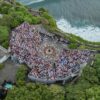 An aerial view of a crowded amphitheater at Uluwatu Temple in Bali, surrounded by lush greenery and ocean views.
