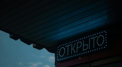 A glowing open sign in Russian under a canopy during nighttime.