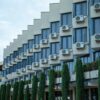 Exterior view of a hotel building featuring rows of windows and air conditioning units, against a clear sky.