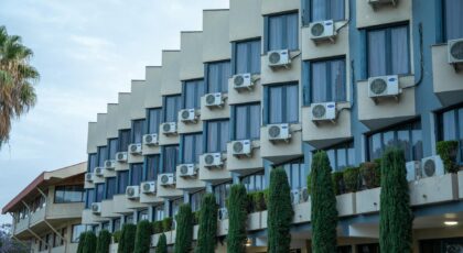 Exterior view of a hotel building featuring rows of windows and air conditioning units, against a clear sky.